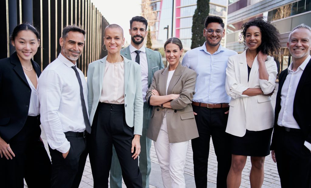 Team portrait multi-ethnic professionals smiling posing with confidence. Young and mature colleagues looking at camera cheerful expression. Group of office workers outside a startup business company.